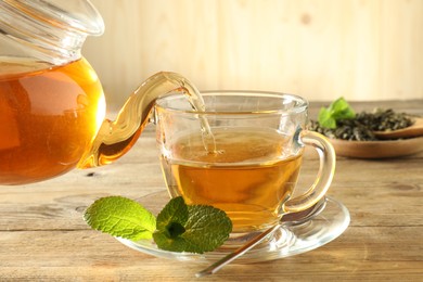 Photo of Pouring freshly brewed tea from teapot into glass cup on wooden table, closeup