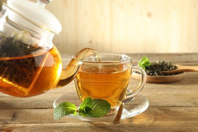 Photo of Pouring freshly brewed tea from teapot into glass cup on wooden table, closeup