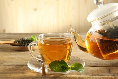 Photo of Pouring freshly brewed tea from teapot into glass cup on wooden table, closeup