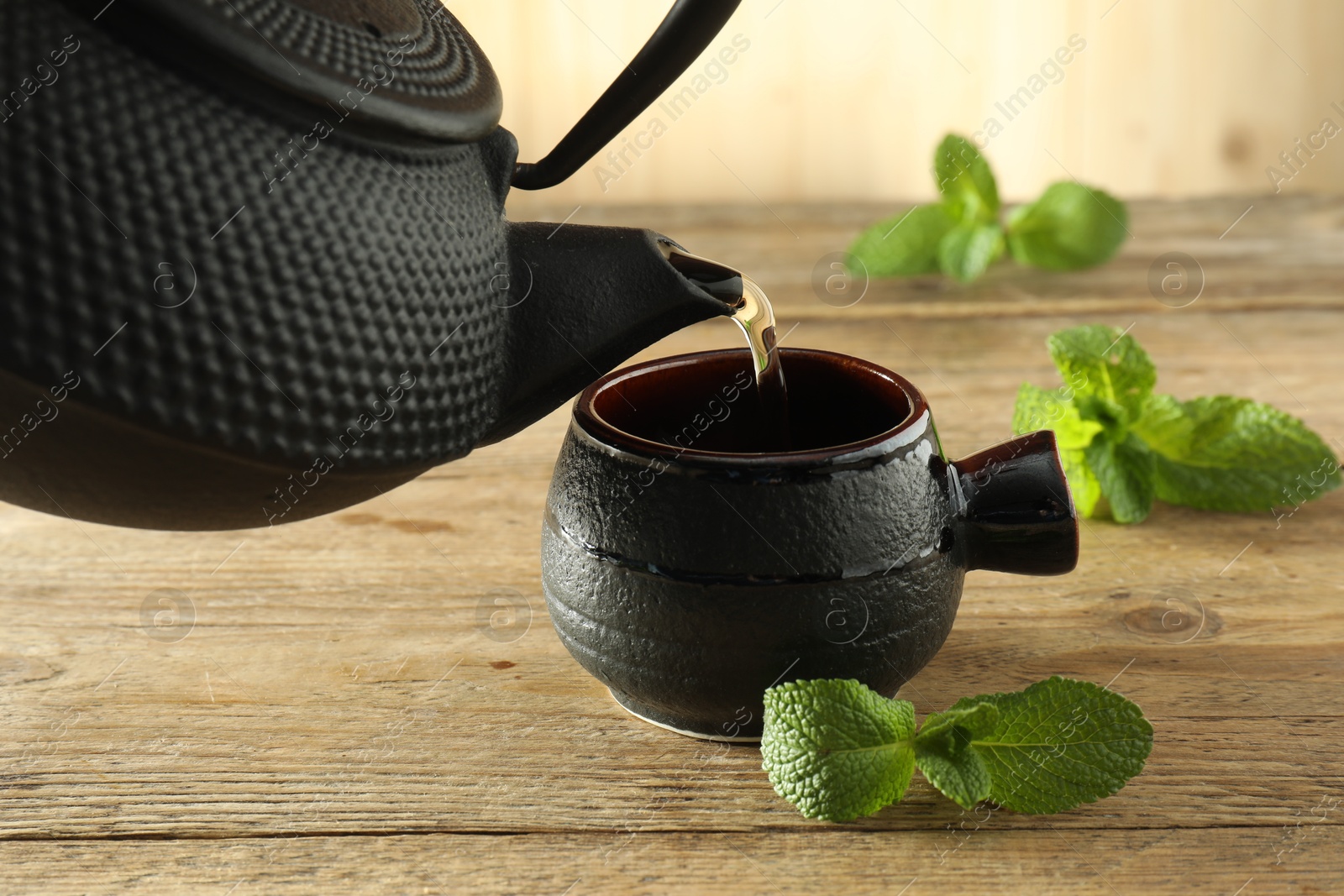 Pouring freshly brewed tea from teapot into ceramic cup on table, closeup Photo of Pouring freshly brewed tea from teapot into ceramic cup on table, closeup