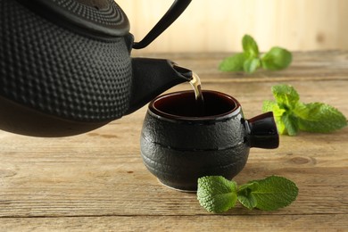 Photo of Pouring freshly brewed tea from teapot into ceramic cup on table, closeup