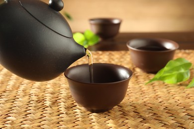 Photo of Pouring freshly brewed tea from teapot into ceramic cup on table, closeup