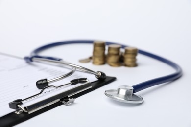 Photo of Stethoscope, medical card form and coins on light background, closeup