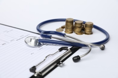 Photo of Stethoscope, medical card form and coins on light background, closeup