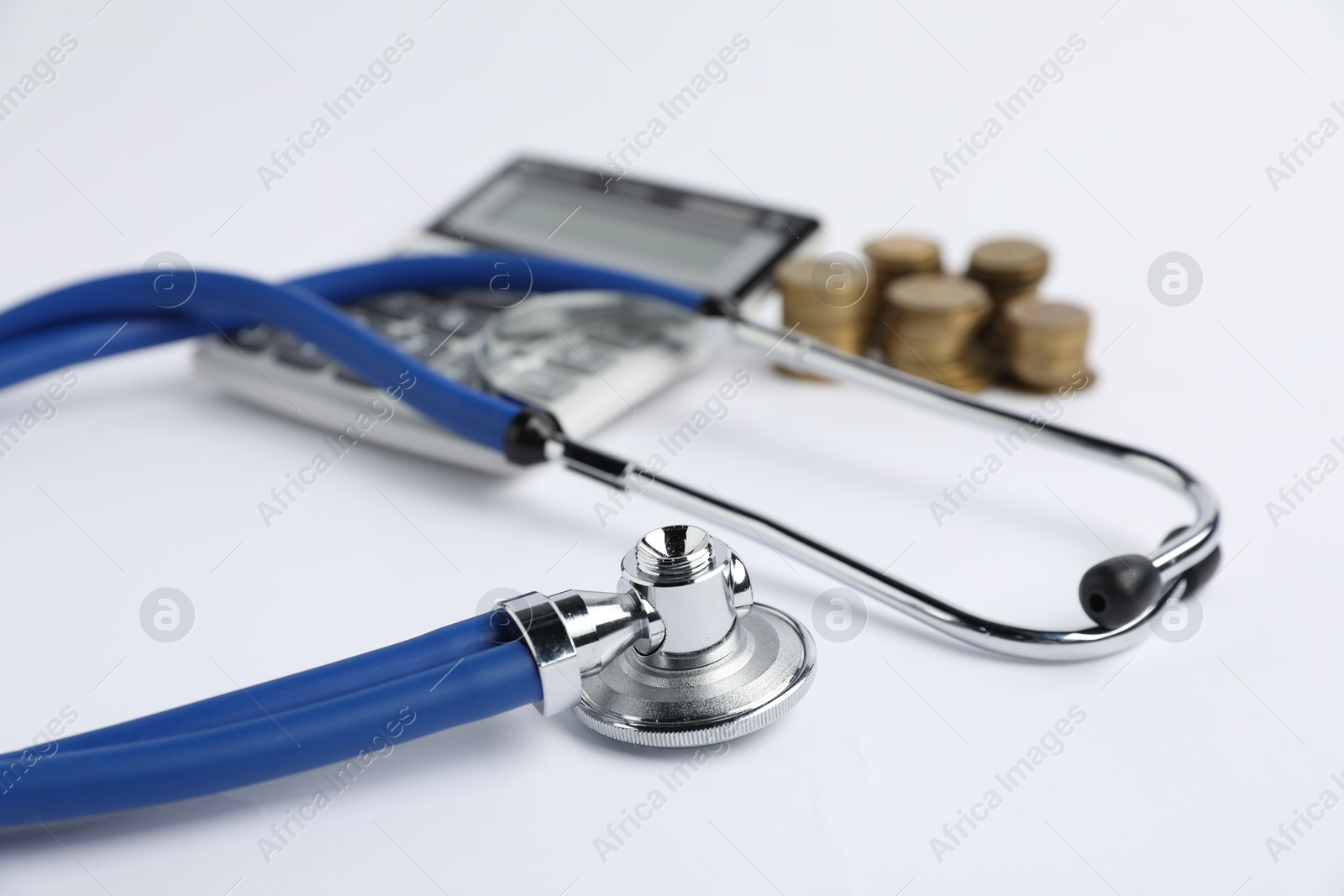 Stethoscope, calculator and coins on light background, closeup Photo of Stethoscope, calculator and coins on light background, closeup