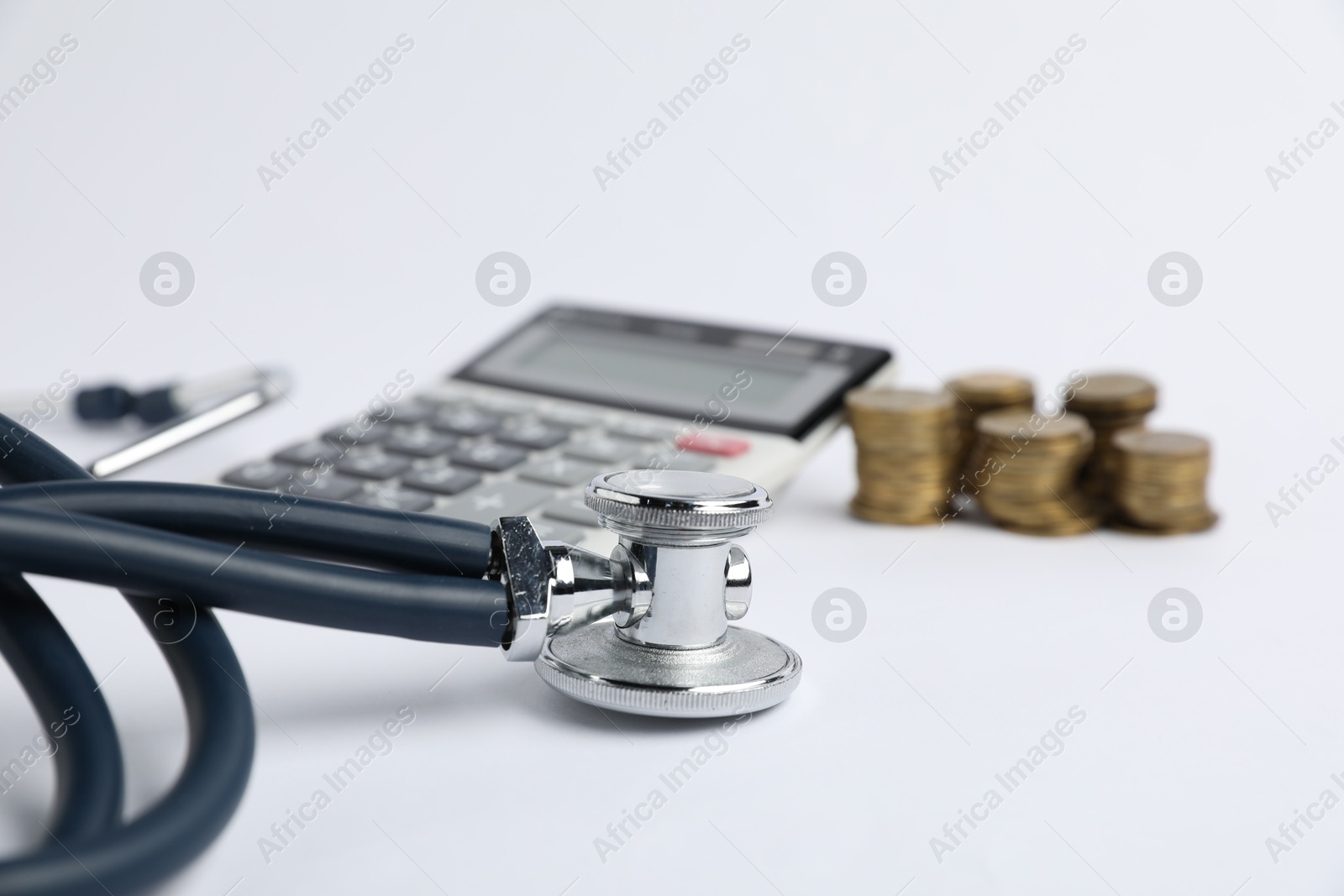 Stethoscope, calculator and coins on light background, closeup Photo of Stethoscope, calculator and coins on light background, closeup