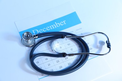 Photo of Stethoscope and calendar on light background, above view