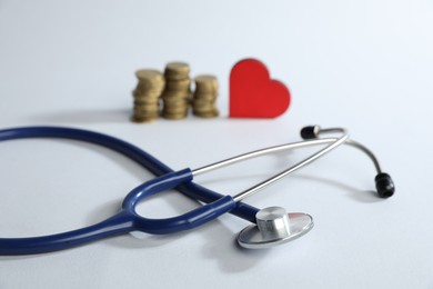 Photo of Stethoscope, red decorative heart and coins on light background, selective focus