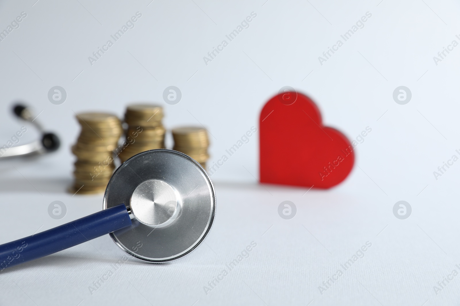 Stethoscope, red decorative heart and coins on light background, selective focus Photo of Stethoscope, red decorative heart and coins on light background, selective focus