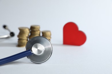Photo of Stethoscope, red decorative heart and coins on light background, selective focus