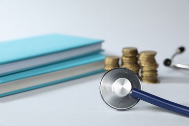 Photo of Stethoscope, books and coins on light background, selective focus