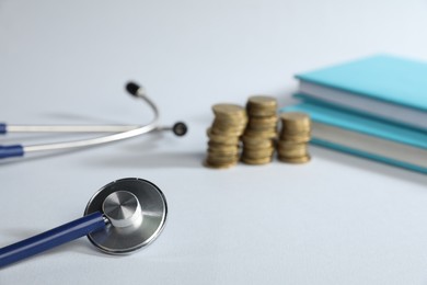 Photo of Stethoscope, books and coins on light background, selective focus