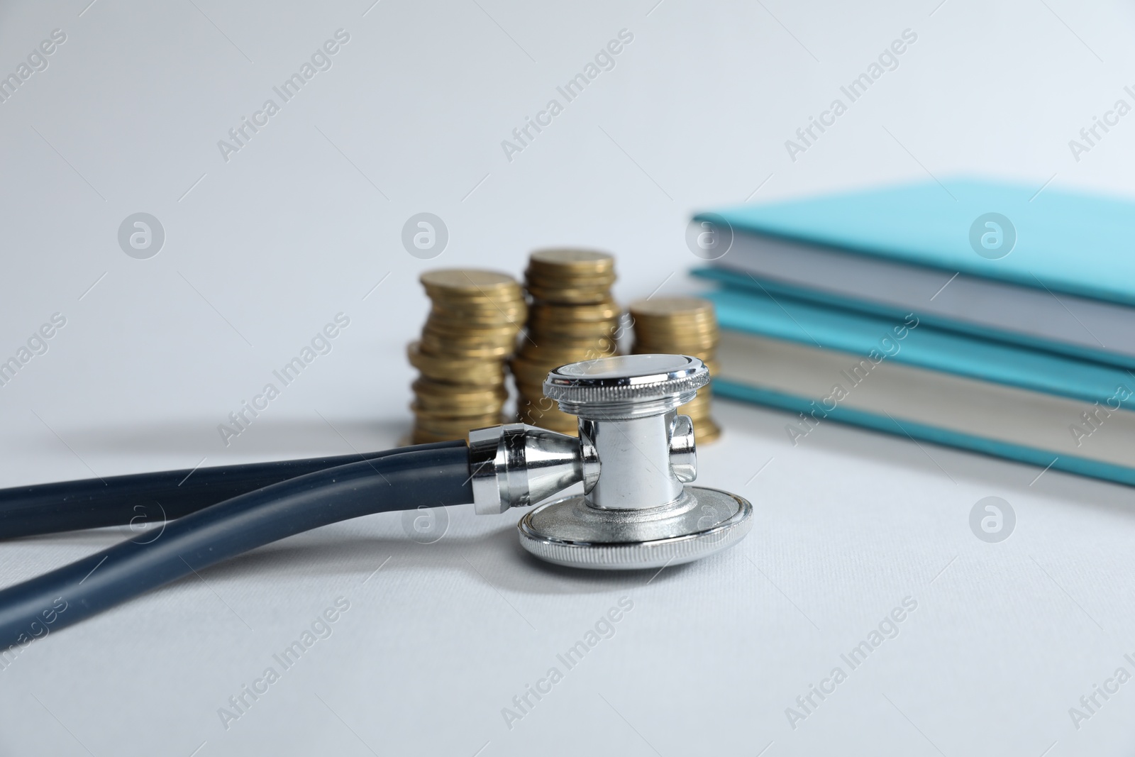 Stethoscope, books and coins on light background, selective focus Photo of Stethoscope, books and coins on light background, selective focus