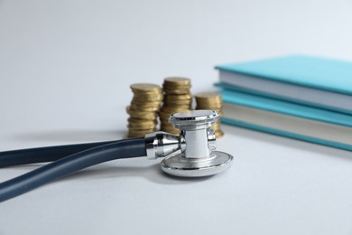Photo of Stethoscope, books and coins on light background, selective focus