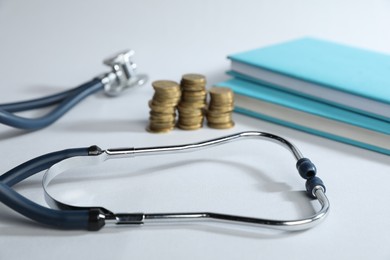 Photo of Stethoscope, books and coins on light background, closeup