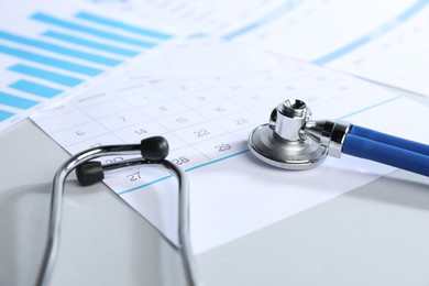 Photo of Stethoscope, calendar and chart on light background, closeup