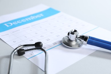 Photo of Stethoscope and calendar on light background, closeup