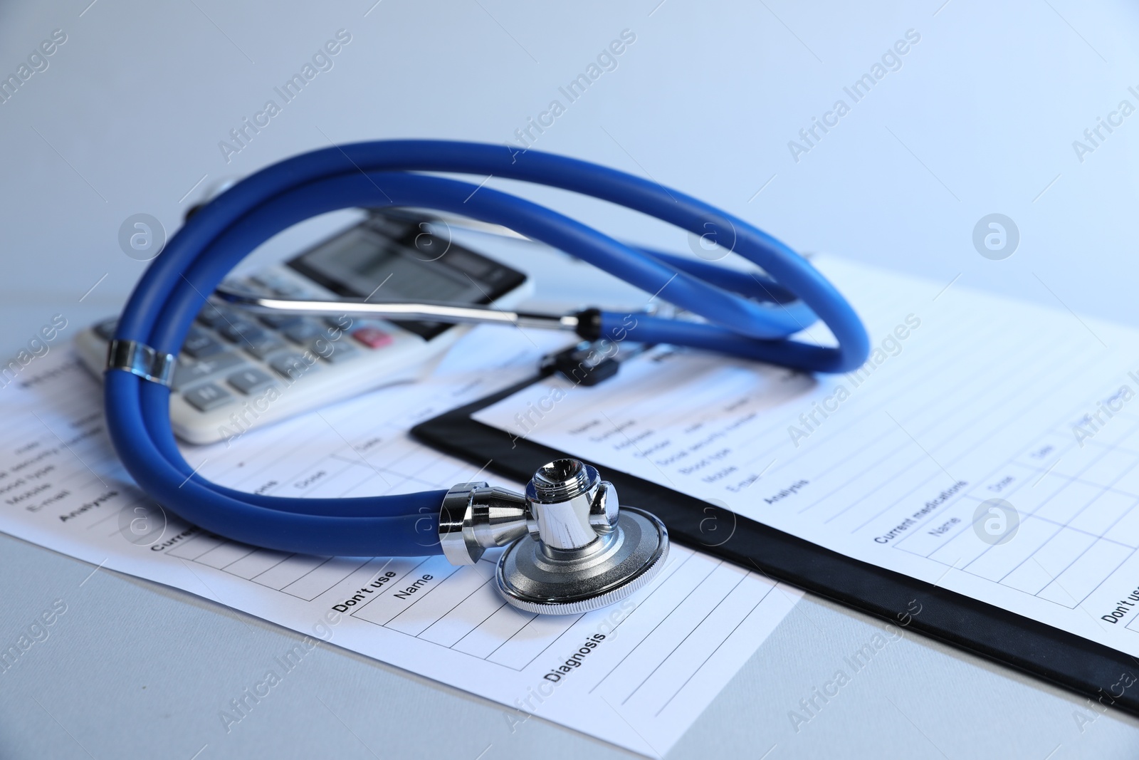 Stethoscope, medical card forms and calculator on light background, closeup Photo of Stethoscope, medical card forms and calculator on light background, closeup