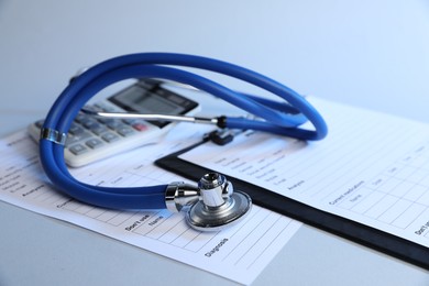 Photo of Stethoscope, medical card forms and calculator on light background, closeup