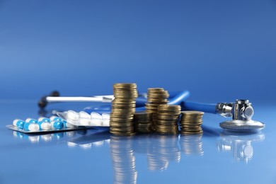 Photo of Stethoscope, pills and coins on glass surface against blue background