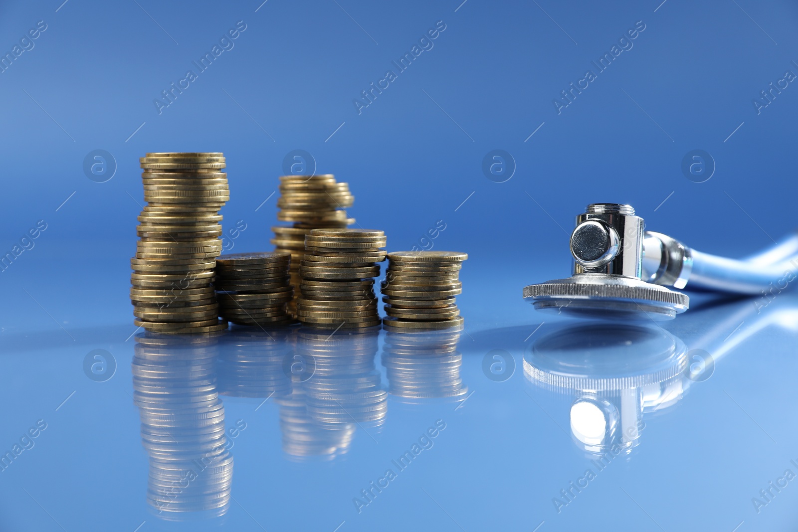 Stethoscope and coins on glass surface against blue background. Medical tool Photo of Stethoscope and coins on glass surface against blue background. Medical tool