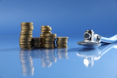 Photo of Stethoscope and coins on glass surface against blue background. Medical tool