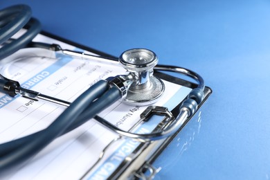 Photo of Stethoscope and medical card form on blue background, closeup