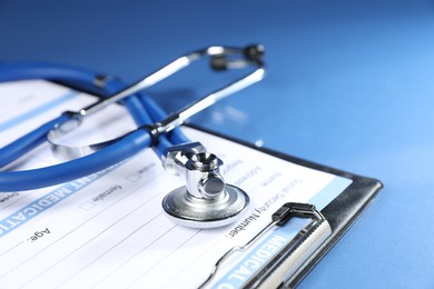 Photo of Stethoscope and medical card form on blue background, closeup