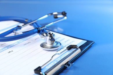 Photo of Stethoscope and medical card form on blue background, closeup