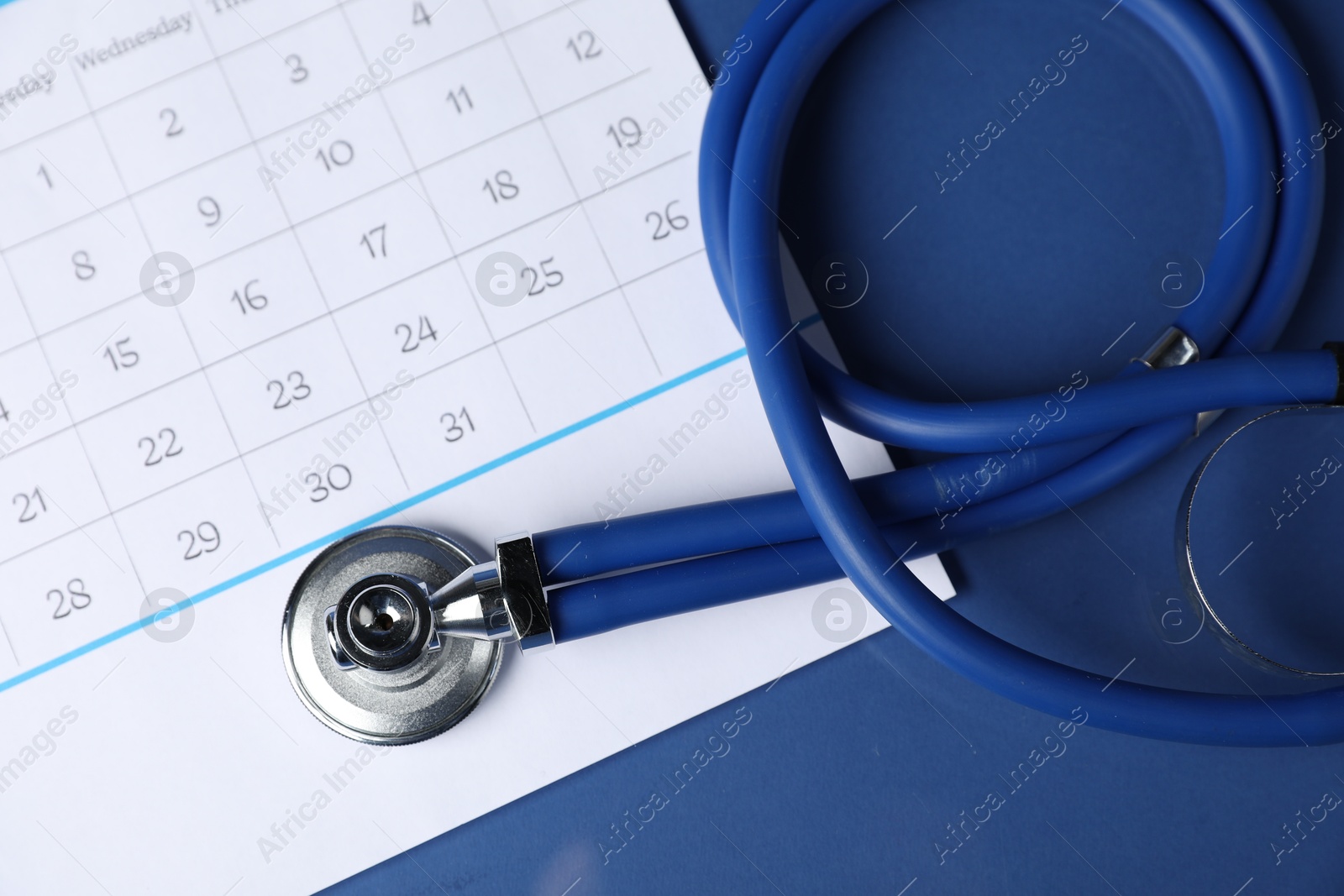 Stethoscope and calendar on blue background, top view Photo of Stethoscope and calendar on blue background, top view