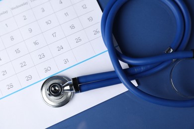 Photo of Stethoscope and calendar on blue background, top view