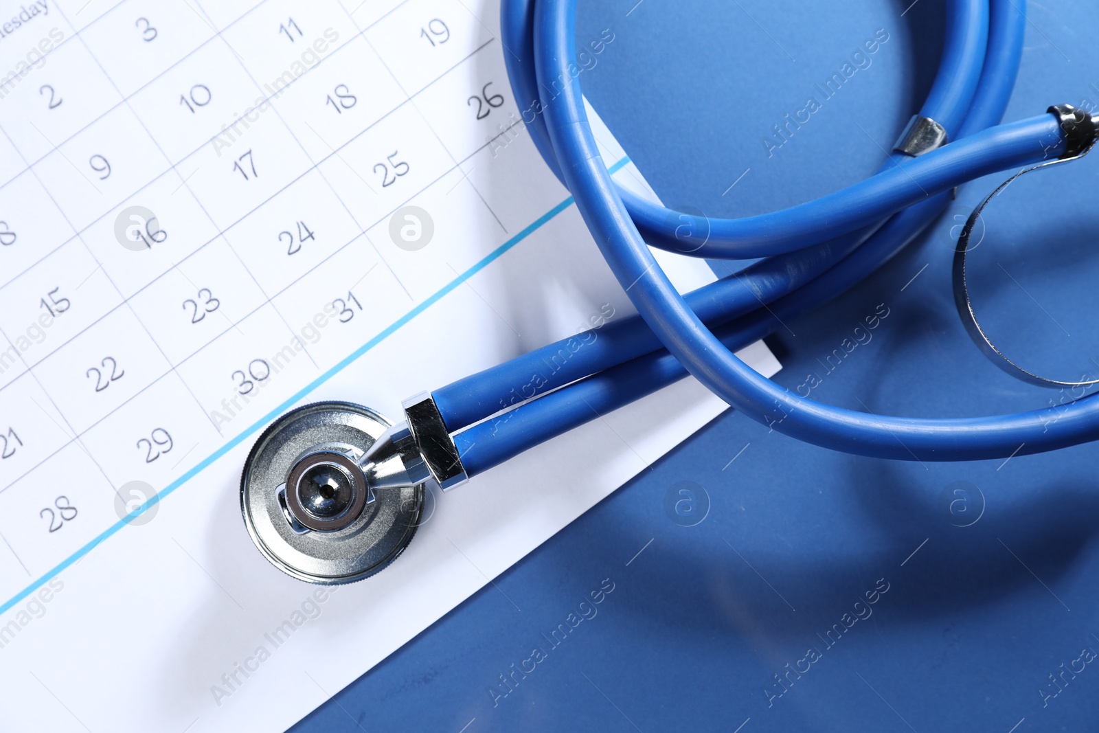 Stethoscope and calendar on blue background, top view Photo of Stethoscope and calendar on blue background, top view