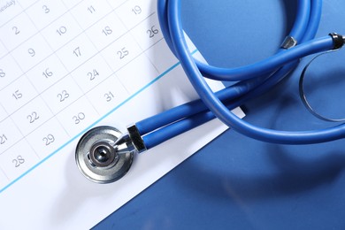 Photo of Stethoscope and calendar on blue background, top view