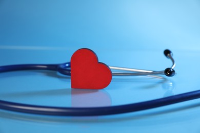 Photo of Stethoscope and red decorative heart on light blue background, closeup