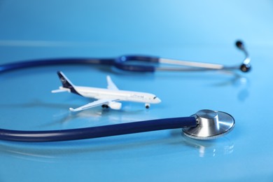 Photo of Stethoscope and airplane model on light blue background, closeup