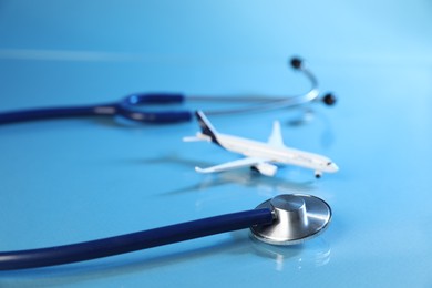 Photo of Stethoscope and airplane model on light blue background, closeup