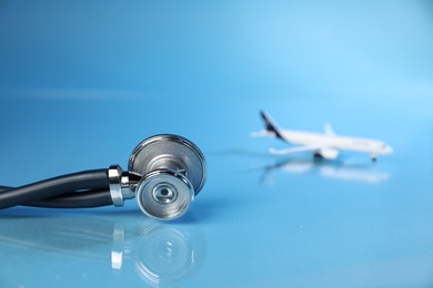 Photo of Stethoscope and airplane model on light blue background, selective focus