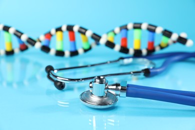 Photo of Stethoscope and DNA structure model on light blue background, closeup