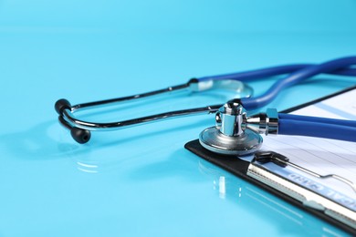 Photo of Stethoscope and medical card form on light blue background, closeup