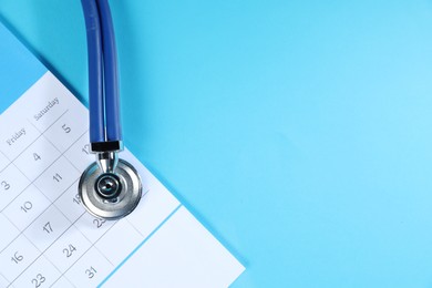 Photo of Stethoscope and calendar on light blue background, top view. Space for text