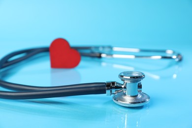 Photo of Stethoscope and red decorative heart on light blue background, closeup