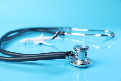 Photo of Stethoscope and airplane model on light blue background, closeup