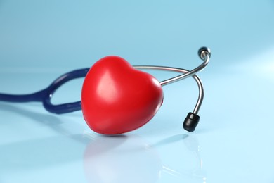 Photo of Stethoscope and red decorative heart on light blue background, closeup