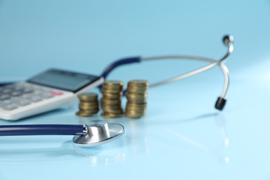 Photo of Stethoscope, calculator and coins on light blue background, closeup
