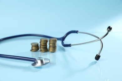 Photo of Stethoscope and coins on light blue background, closeup