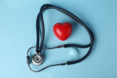 Photo of Stethoscope and red decorative heart on light blue background, top view