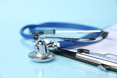 Photo of Stethoscope and medical card form on light blue background, closeup