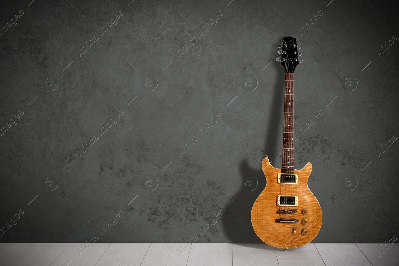 Image of Modern electric guitar on floor near grey grunge wall. Space for text