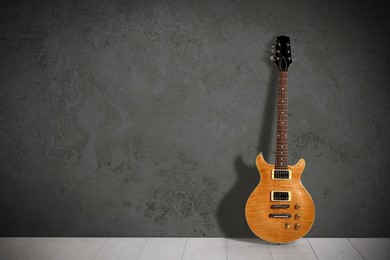 Image of Modern electric guitar on floor near grey grunge wall. Space for text