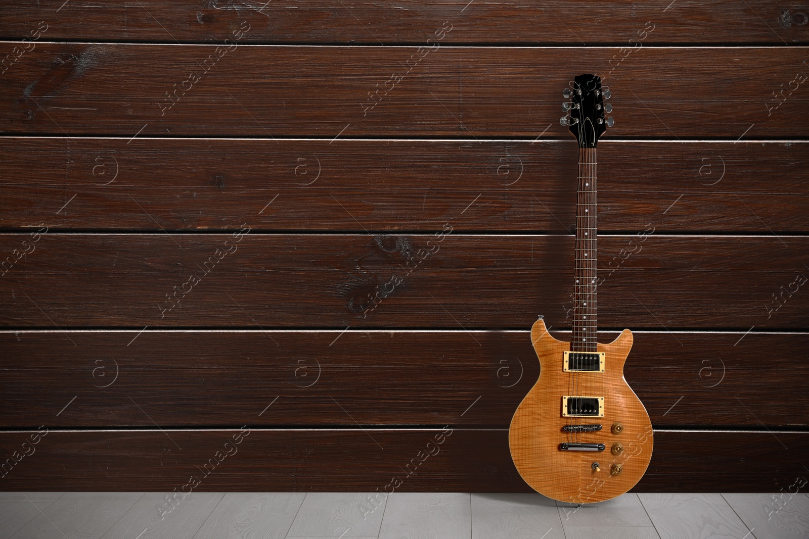 Image of Modern electric guitar on floor near wooden wall. Space for text